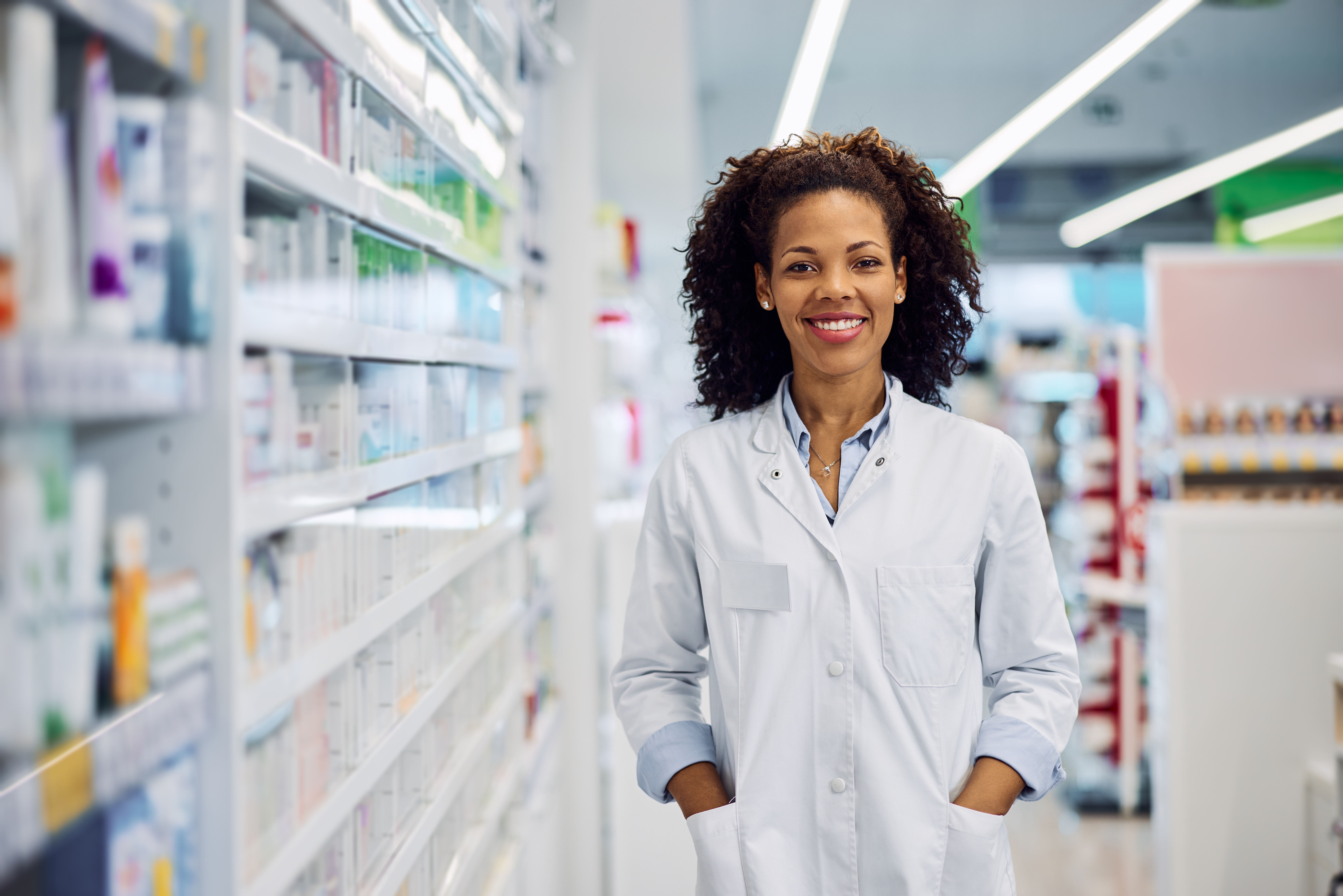 A female pharmacist with curly hair smiling at the pharmacy.
