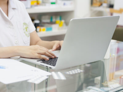 Pharmacist typing on a laptop and medication on the counter at the pharmacy.