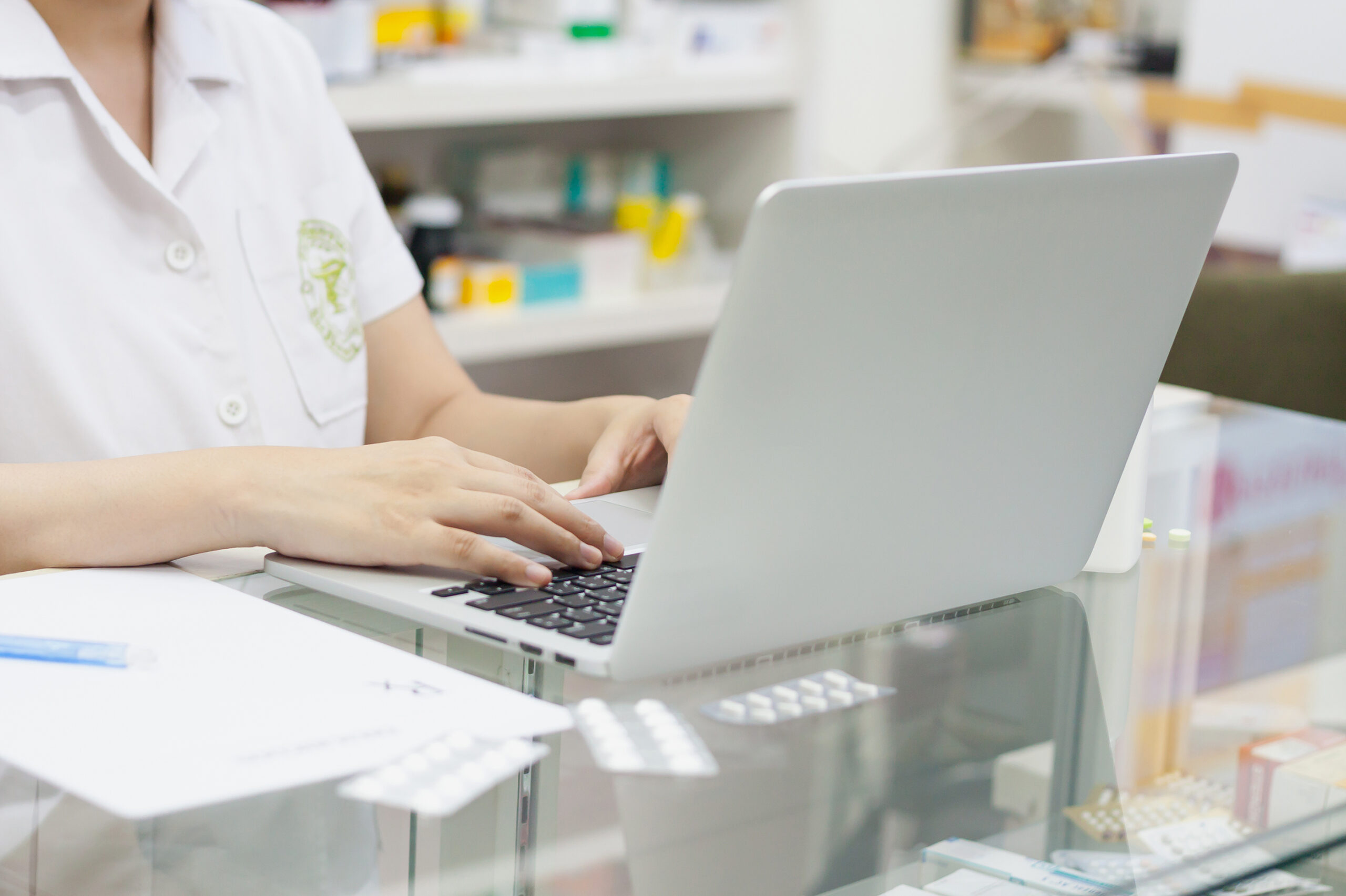 Pharmacist typing on a laptop and medication on the counter at the pharmacy.