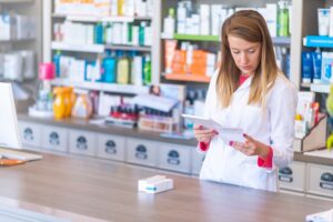 A young female pharmacist looking at a tablet and prescription.