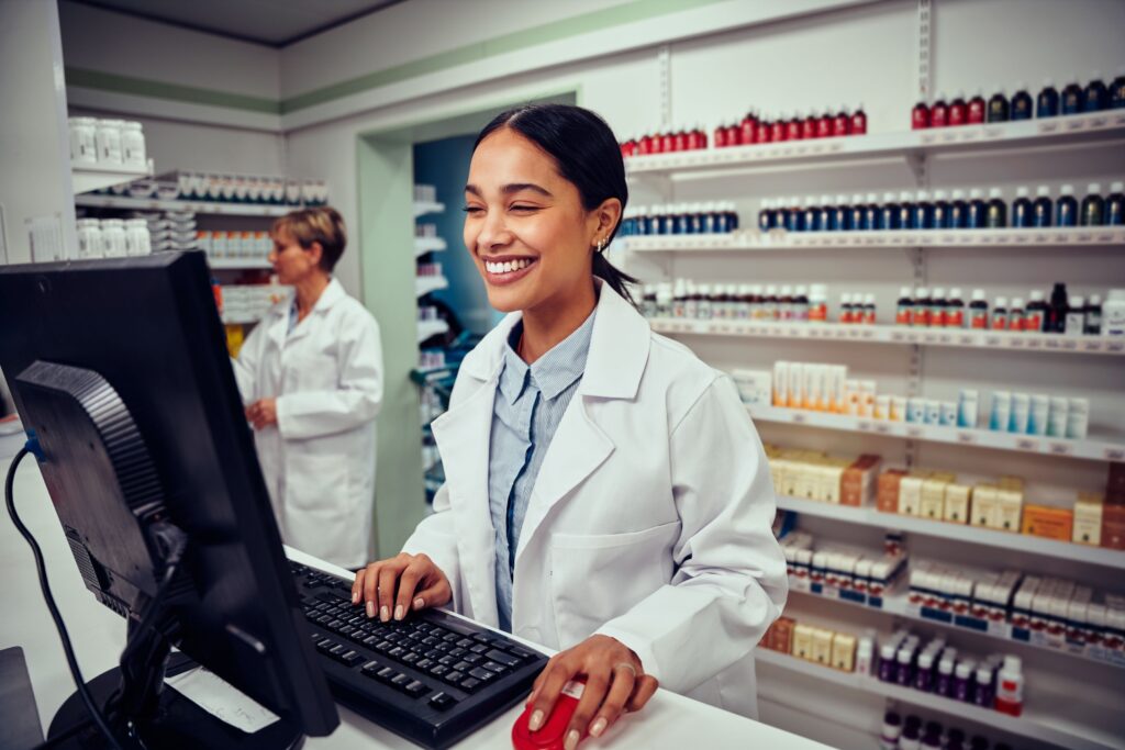 A cheerful young female pharmacist working on a computer.