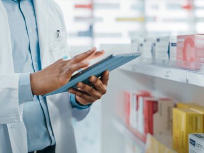 Male pharmacist holding a tablet with pharmacy in the background.