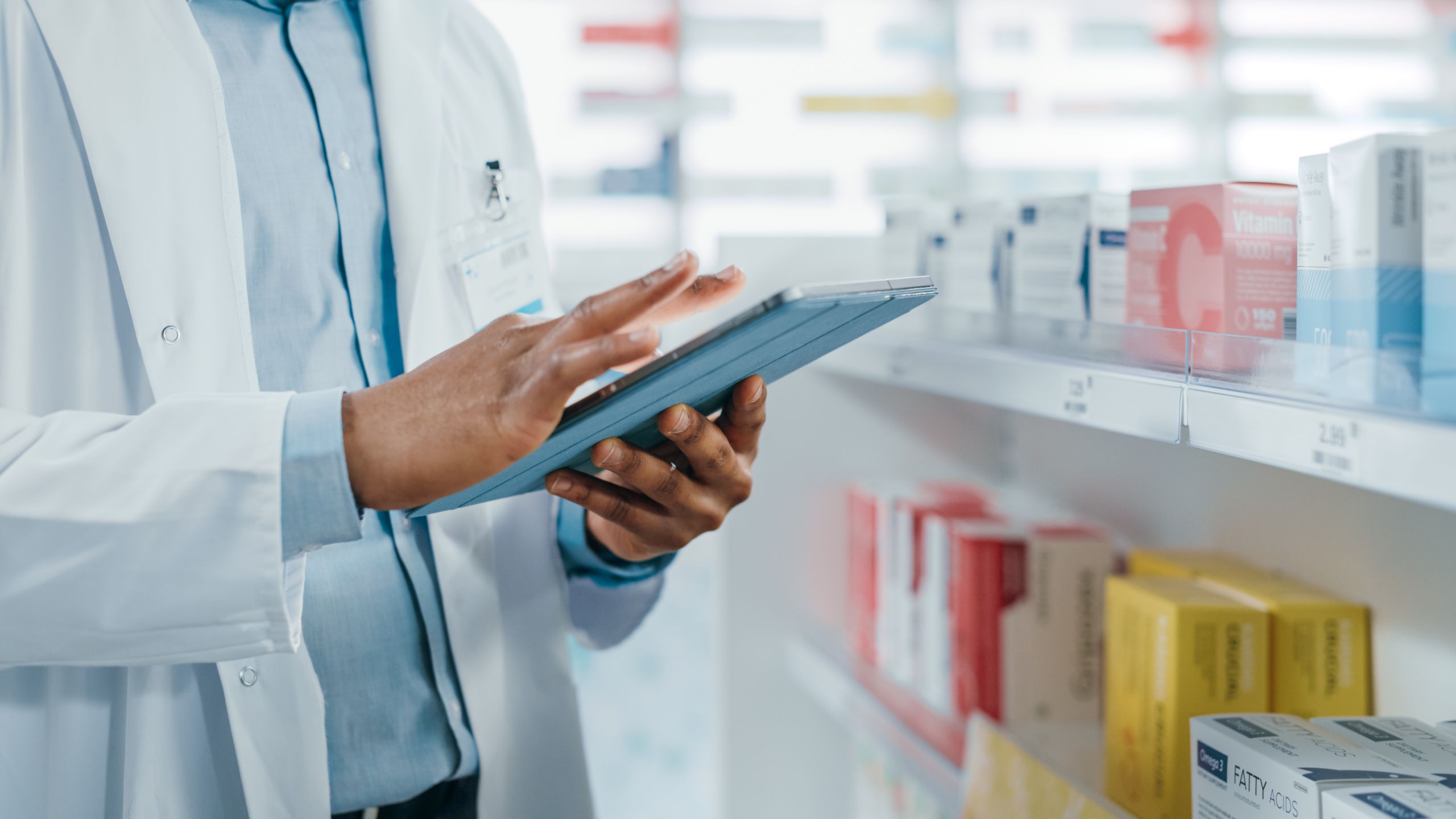 Male pharmacist holding a tablet with pharmacy in the background.