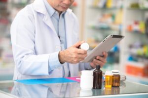 Male pharmacist looking at a tablet and prescription.