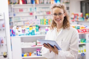 Female pharmacist holding a tablet with the pharmacy in the background.