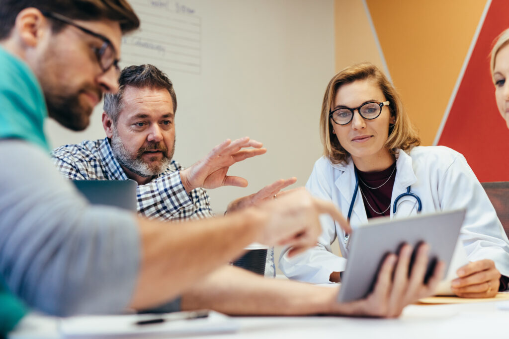 A female doctor and group of people looking at a tablet while sitting at a table.