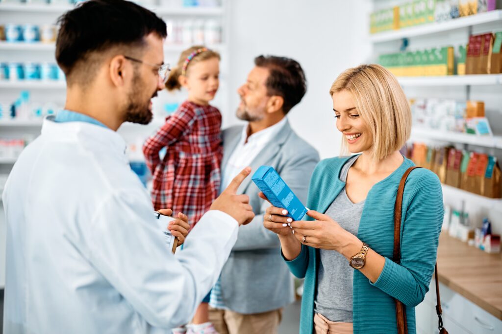 A male pharmacist helping a woman while her husband and daughter are in the background.