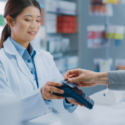 A female pharmacist taking a contactless payment from a customer.