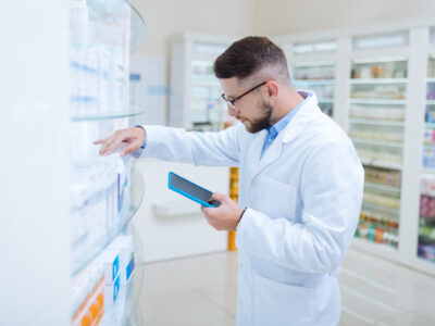 A young male pharmacist checking inventory on a tablet.
