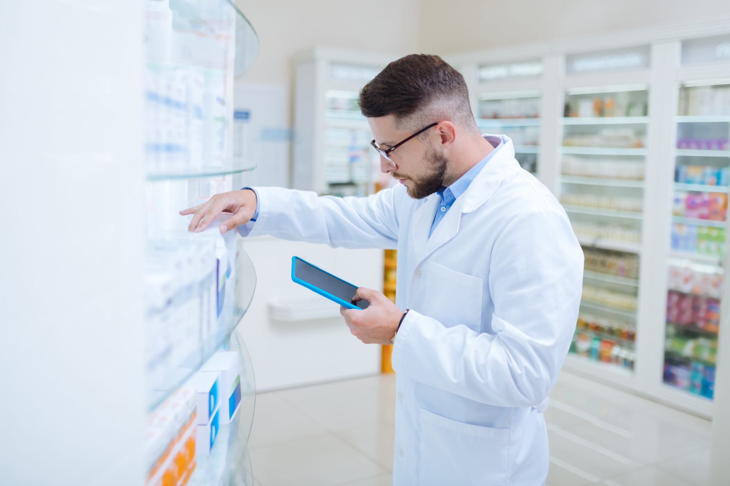 A young male pharmacist checking inventory on a tablet.