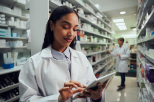 Female pharmacist looking at tablet with the pharmacy in the background.