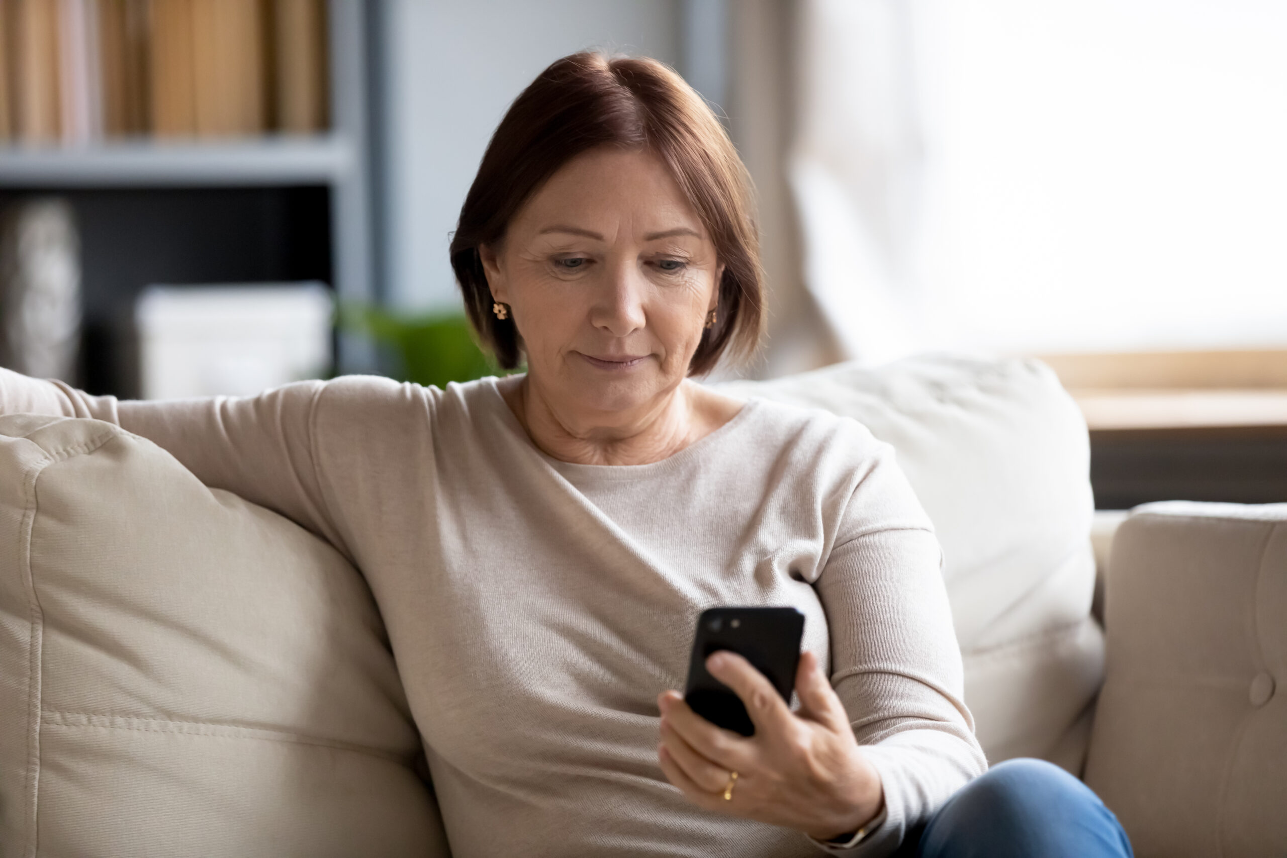 Middle aged woman sitting on couch looking at a smart phone.