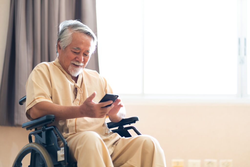 Elderly man sitting in a wheelchair looking at his smartphone.