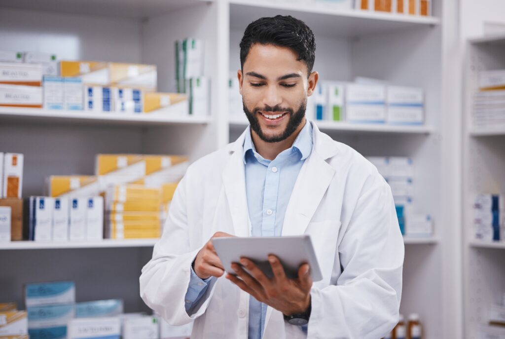 Male pharmacist looking at a tablet with pharmacy in the background.