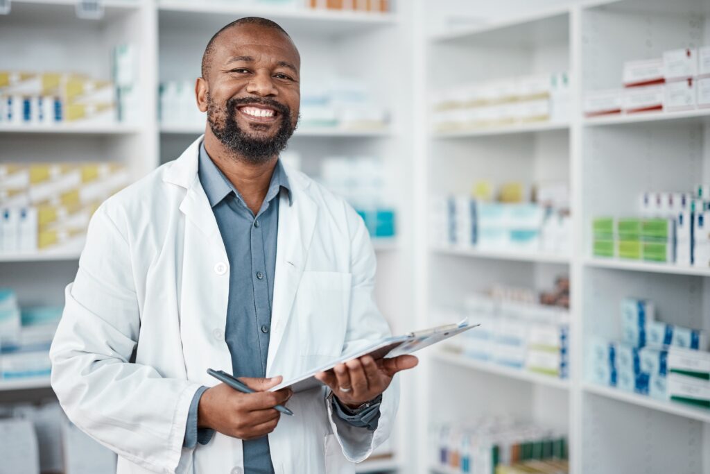 A male pharmacist holding a clipboard at a pharmacy.