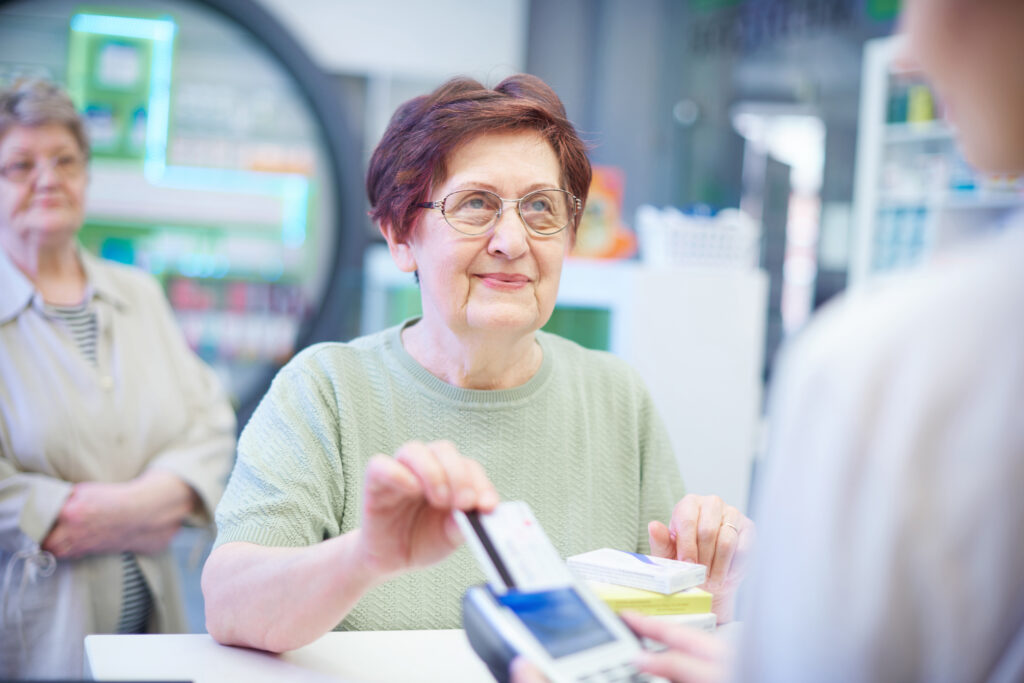 A elderly woman using a credit card to pay at a pharmacy.