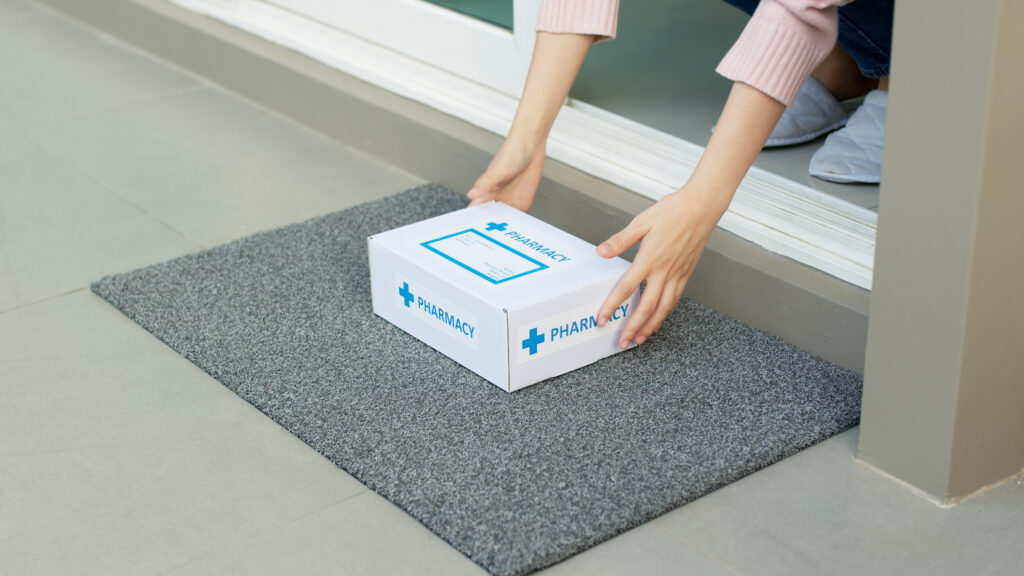 A woman picking up a med delivery from her front door.