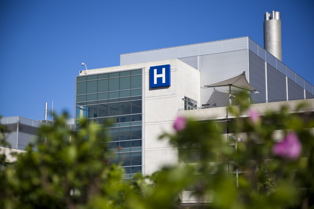 Modern hospital with blue H sign with a clear blue sky.