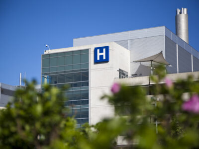 Modern hospital with blue H sign with a clear blue sky.