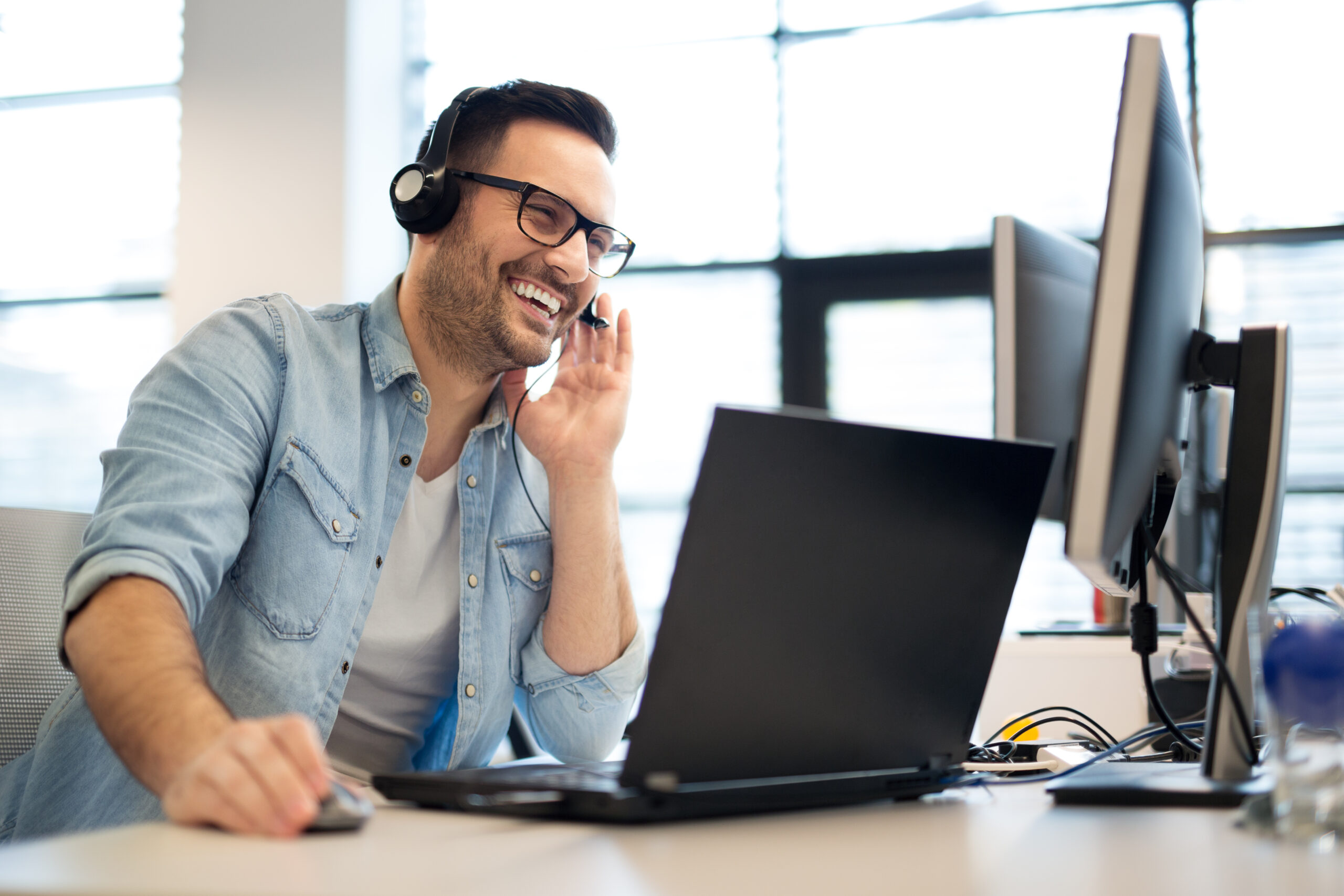 Man smiling sitting in front of computer talking on headset.