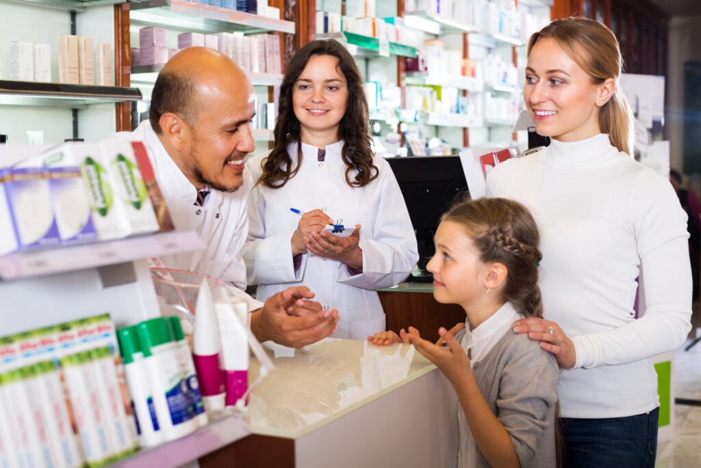 Two smiling pharmacists helping a woman and a girl at a pharmacy.