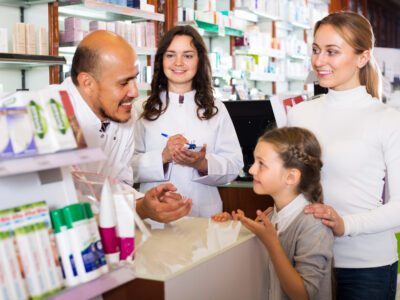 Two smiling pharmacists helping a woman and a girl at a pharmacy.