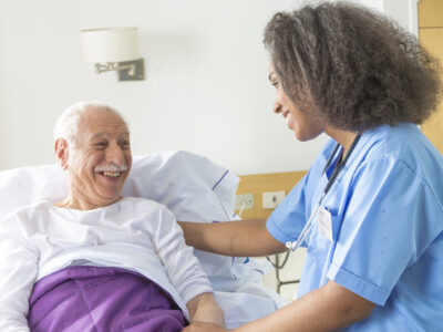 A female doctor visiting an elderly male patient in hospital room.