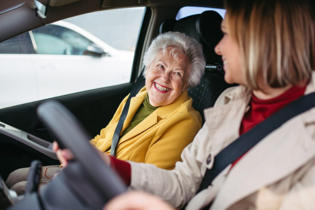 Elderly woman smiling looking at younger woman in side a car