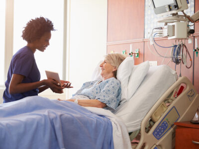 Pharmacy tech showing tablet to elderly patient at bedside