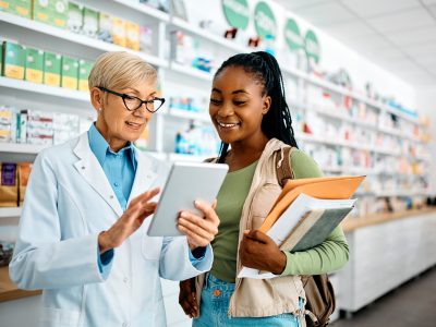 Older pharmacist holding tablet helping younger patient